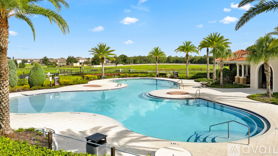 A large outdoor swimming pool surrounded by palm trees and a building in the background.