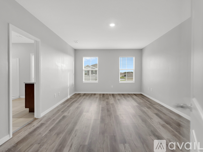 A spacious room with wooden flooring and two windows.