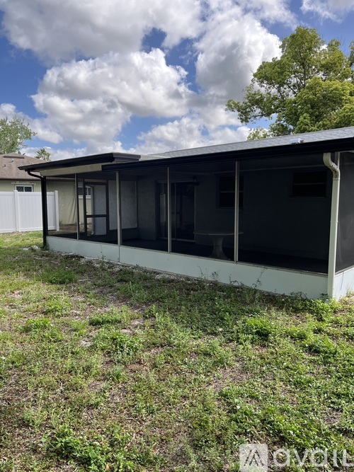 A small building with a metal roof and a white fence is surrounded by grass and weeds.