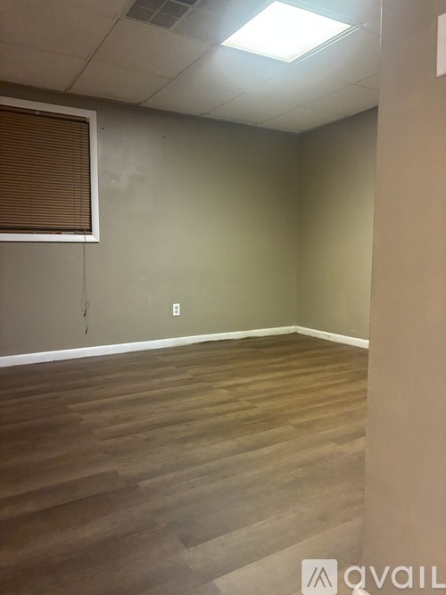 A room with wooden flooring and a window with blinds.