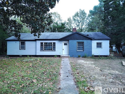 A small house with a white and blue exterior is surrounded by trees and grass.