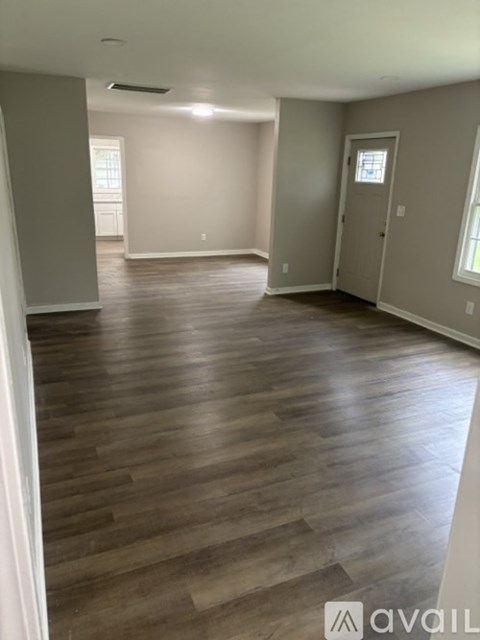 A spacious room with wooden flooring and a door on the right.