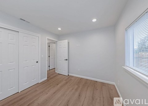 A room with white walls and wooden flooring, featuring a white door and a window with blinds.