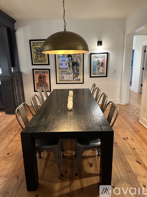 A long wooden table with chairs and a hanging light fixture in a room with wooden floors and framed pictures on the wall.