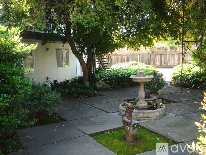 A garden with a fountain and a house in the background.