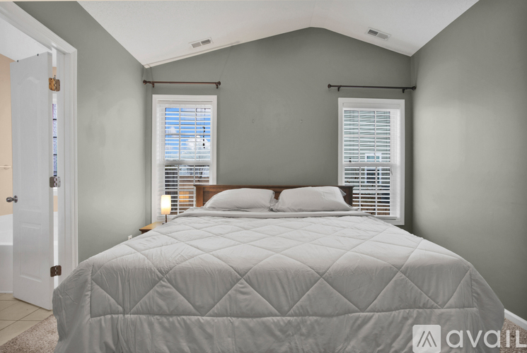 A bedroom with a large bed and a window with blinds.