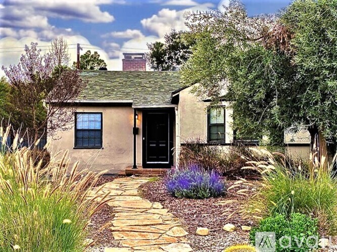 A small house with a black door and a stone pathway leading to it.