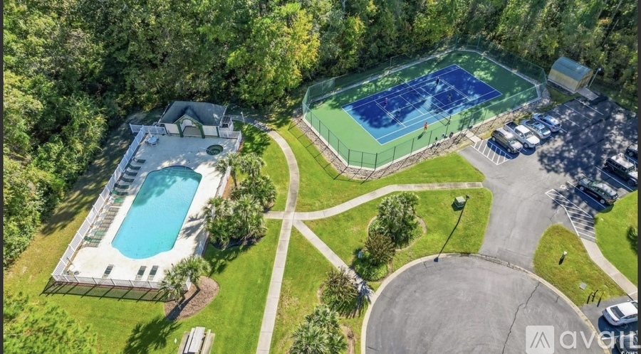 An aerial view of a tennis court, swimming pool, and parking lot.