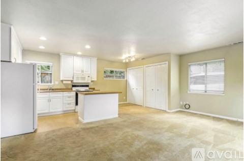 A kitchen with white appliances and cabinets, a countertop, and a window with blinds.