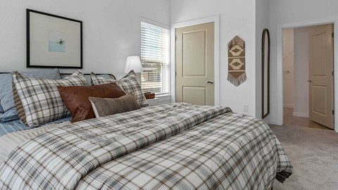 A bedroom with a bed covered in a plaid comforter and pillows.