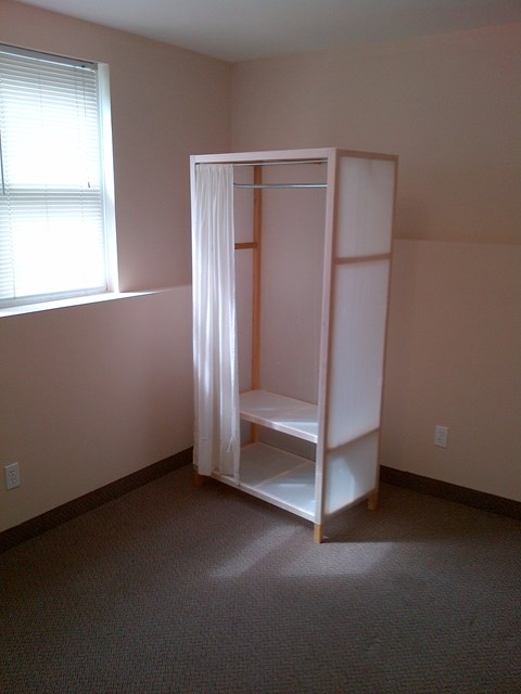 A white closet with a shelf is in a room with a window.