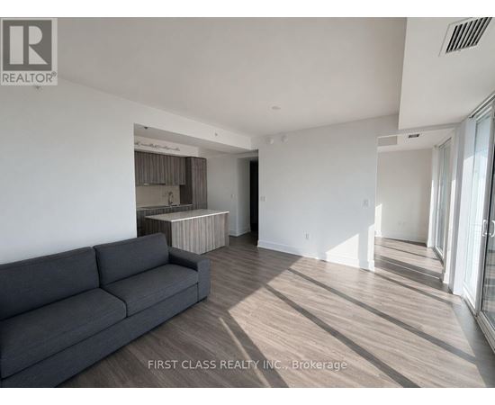 A grey couch sits in a spacious living room with wood flooring and white walls.