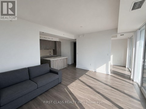 A grey couch sits in a spacious living room with wood flooring and white walls.