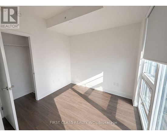 A room with a wooden floor and white walls, with a door on the left and a window on the right.