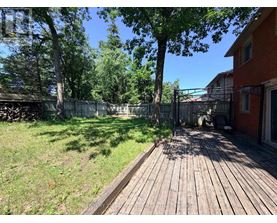 A wooden deck leads to a backyard with a fence and trees.