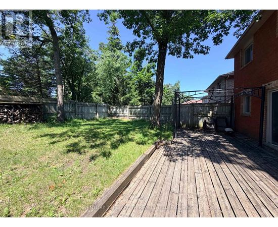 A wooden deck leads to a backyard with a fence and trees.