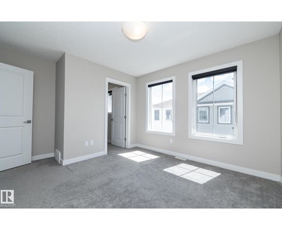 A spacious room with a carpeted floor and three windows.