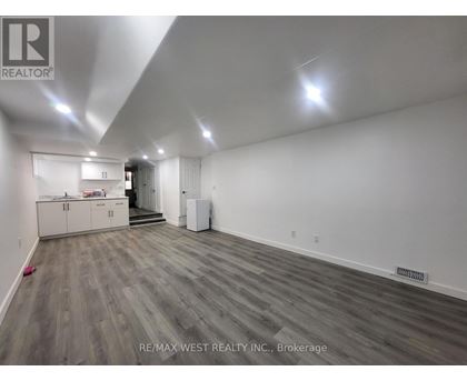 A spacious room with wood flooring and white walls, furnished with a kitchenette.