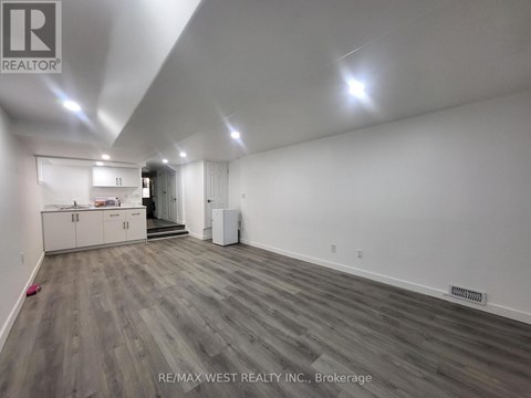 A spacious room with wood flooring and white walls, furnished with a kitchenette.