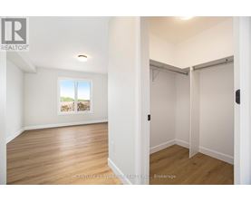A room with wooden floors and white walls, with a window showing a view of trees and a wall with a picture of a house.