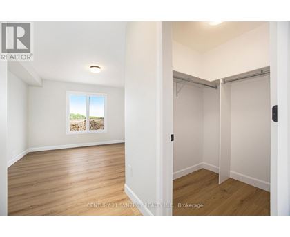 A room with wooden floors and white walls, with a window showing a view of trees and a wall with a picture of a house.