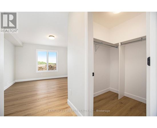 A room with wooden floors and white walls, with a window showing a view of trees and a wall with a picture of a house.