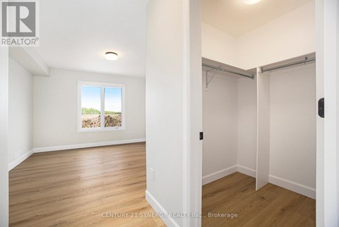 A room with wooden floors and white walls, with a window showing a view of trees and a wall with a picture of a house.