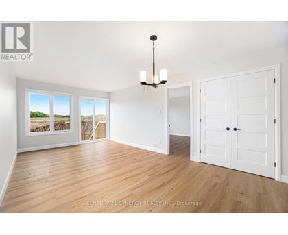 A Synergy Realty Inc. brokerage logo is displayed on a wall in a spacious room with hardwood floors and white walls.