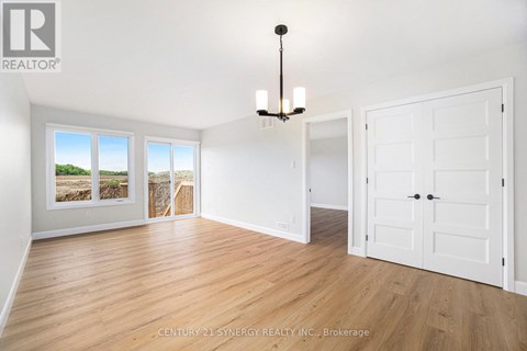 A Synergy Realty Inc. brokerage logo is displayed on a wall in a spacious room with hardwood floors and white walls.
