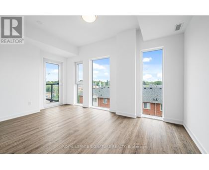 A white room with wooden floors and three windows showing a view of a cityscape.