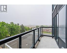 A balcony with glass railings overlooks a view of buildings and trees.