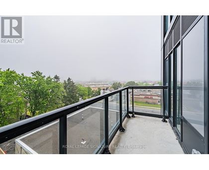 A balcony with glass railings overlooks a view of buildings and trees.
