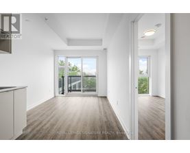 A spacious room with wooden flooring and white walls, with a sliding glass door leading to a balcony.