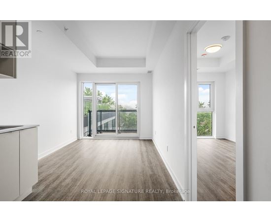 A spacious room with wooden flooring and white walls, with a sliding glass door leading to a balcony.