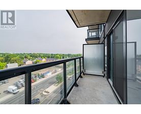 A balcony with a glass door and a view of a highway and trees.