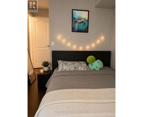 A bedroom with a bed, a small table with a plant and a candle, and a painting on the wall.