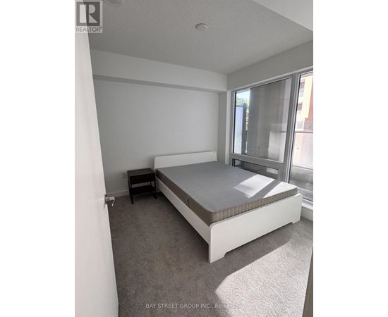 A bedroom with a bed, nightstand, and window.