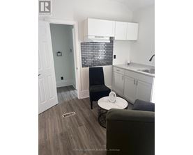 A black chair sits in a kitchen with white cabinets and a black and white tiled backsplash.