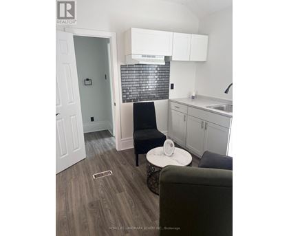 A black chair sits in a kitchen with white cabinets and a black and white tiled backsplash.