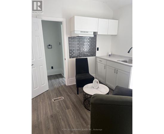 A black chair sits in a kitchen with white cabinets and a black and white tiled backsplash.