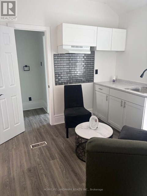 A black chair sits in a kitchen with white cabinets and a black and white tiled backsplash.