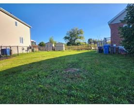 A backyard with a fence and a blue trash can.