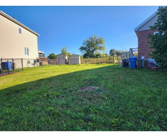 A backyard with a fence and a blue trash can.