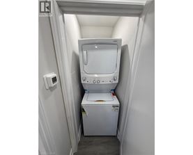 A small white laundry machine sits in a narrow space between a wall and a door.