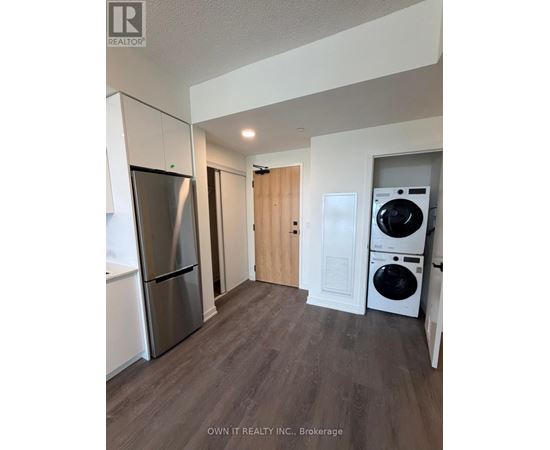 A kitchen with a refrigerator, washing machine and a doorway leading to another room.