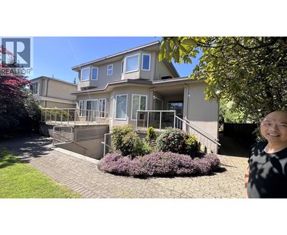 A woman stands in front of a house with a garden.