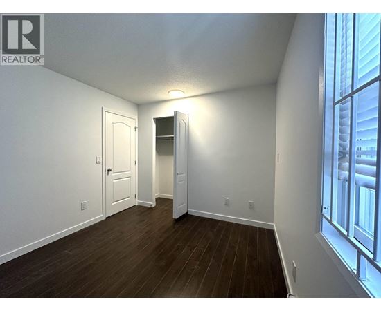 A room with a wooden floor and white walls, with a doorway leading to another room.