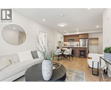 A modern living room with a grey sofa, a round table with a vase on it, and a kitchen area in the background.