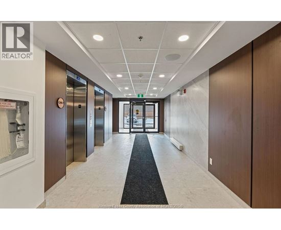 A hallway with a black carpet in the middle and elevators on the left.