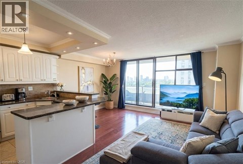 A well-lit, spacious living room with a grey sofa and a kitchen area with white cabinets.